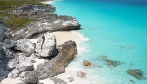 An aerial view of a beach with turquoise water and rocky cliffs. Book a charter flight to the Bahamas for this breathtaking sight.