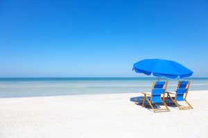 Two chairs on a beach under a blue umbrella in the Bahamas.