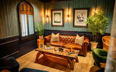 A cozy living room with a brown leather sofa, wooden coffee table, green armchair, plants, wall art, and warm lighting—perfect for relaxing after your adventures on charter flights in Florida and The Bahamas with Ascend Via Makers Air.