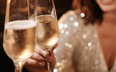 Two people toast with glasses of sparkling wine at a social gathering. One person, wearing a sequined outfit, talks about their recent adventures with charter flights in Florida and The Bahamas via Ascend Via Makers Air.