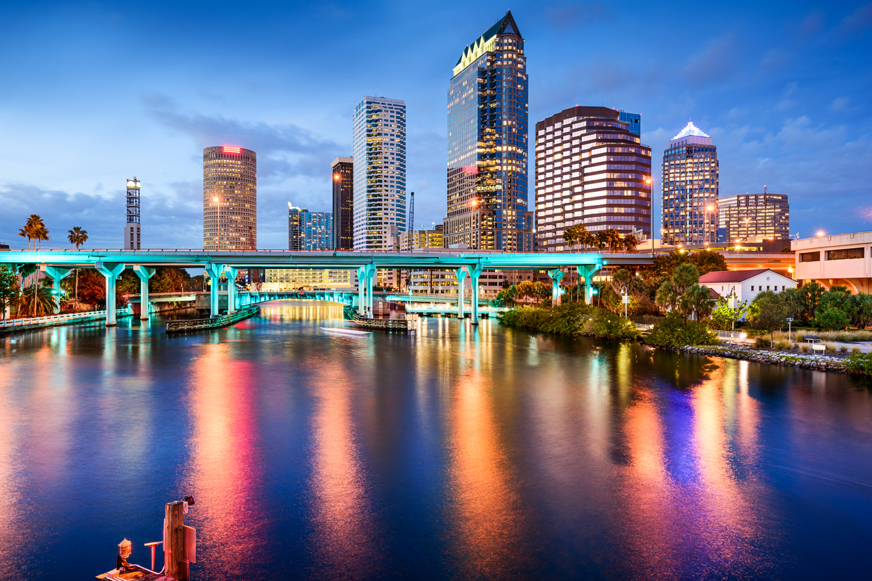 Charter flights to the Bahamas and in Florida City skyline at dusk with illuminated buildings reflected in the water below a bridge. Charter a plane to the Bahamas or in Florida