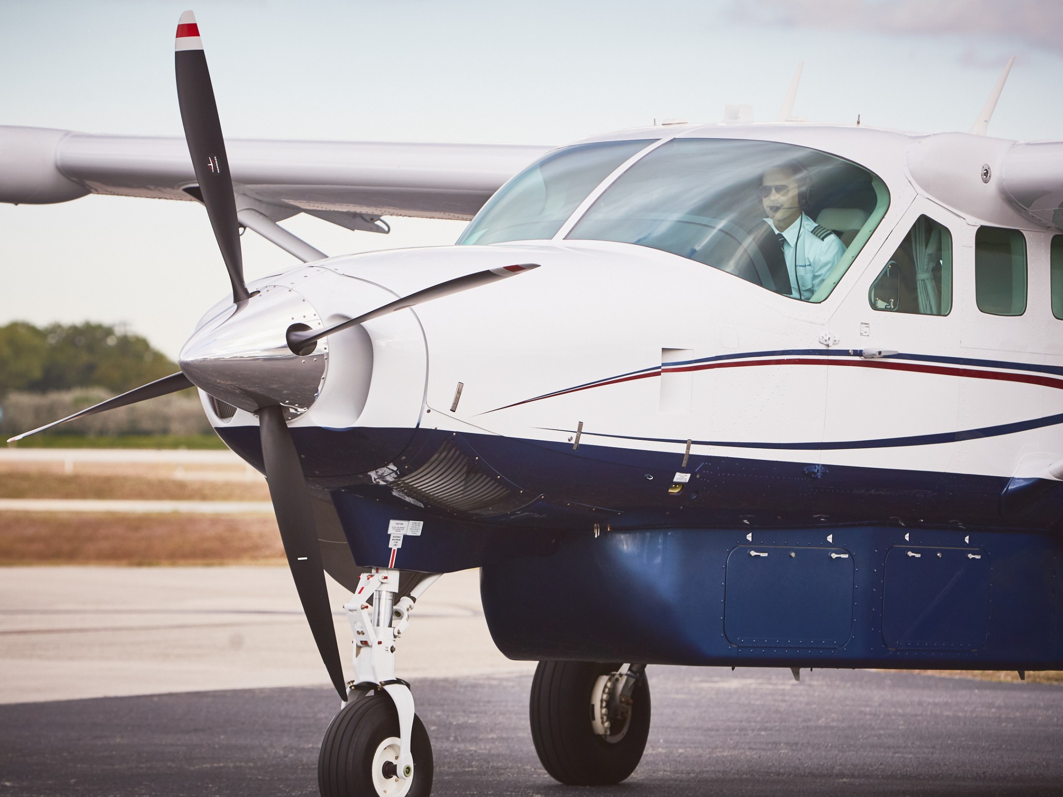 Small propeller plane taxiing on runway with pilot visible in cockpit.