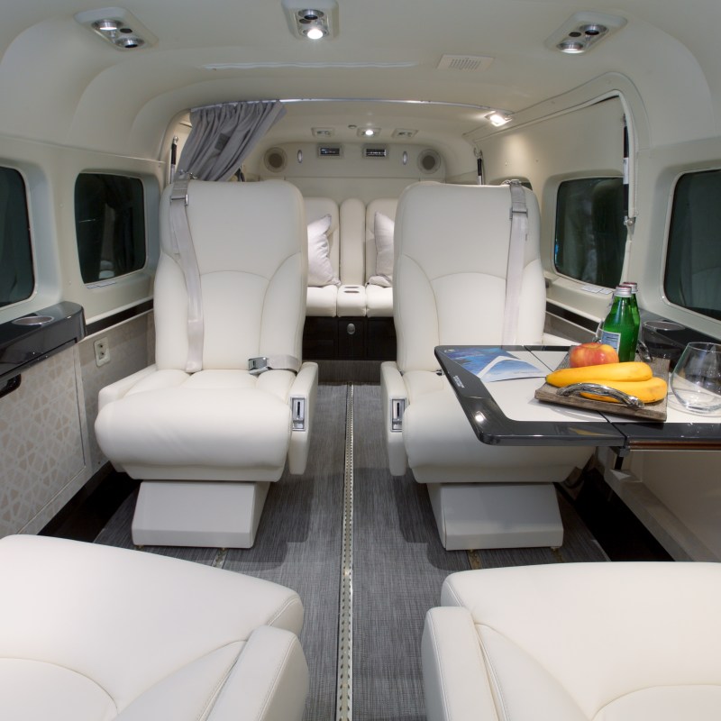 Luxury private jet interior with white leather seats, table with fruit and drinks.
