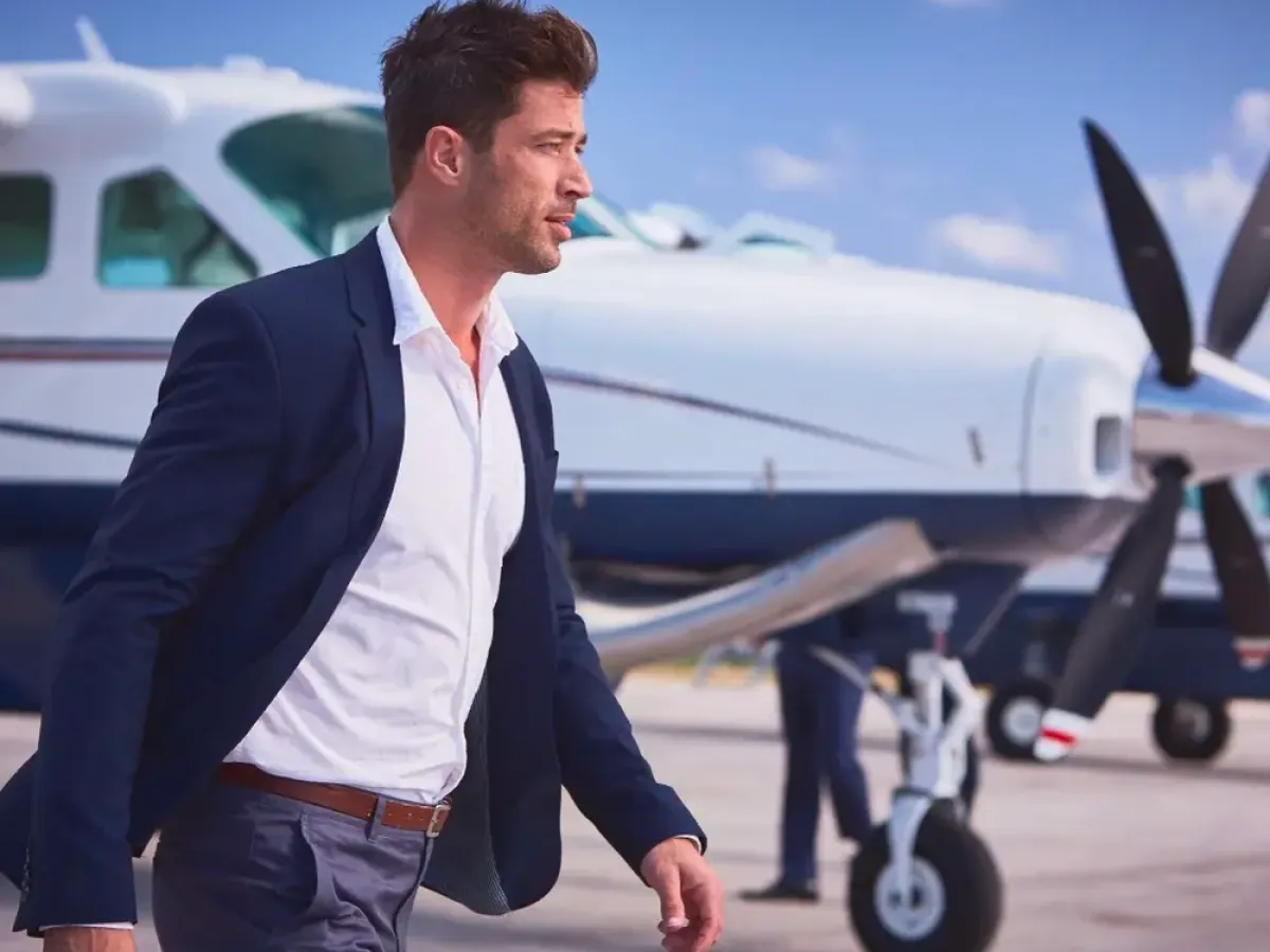 Man in suit walking on tarmac beside a small airplane with blue sky background.
