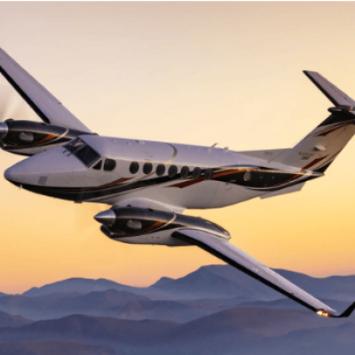 Small airplane flying over mountains at sunset.